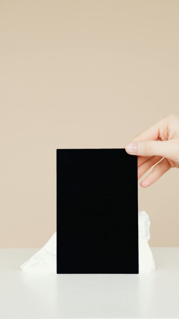 A hand holding a blank black card against a beige minimalist background, ready for mockup.